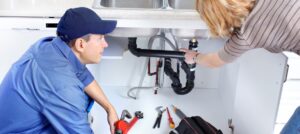 Heating - Bill Howe Plumber vs. technician. A plumber looks under the sink to find a leak.