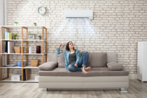 Happy Young Woman Holding Remote Control Relaxing Under The Air Conditioner